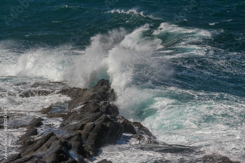 Powerful ocean wave breaks against a rocky shoreline on a sunny day