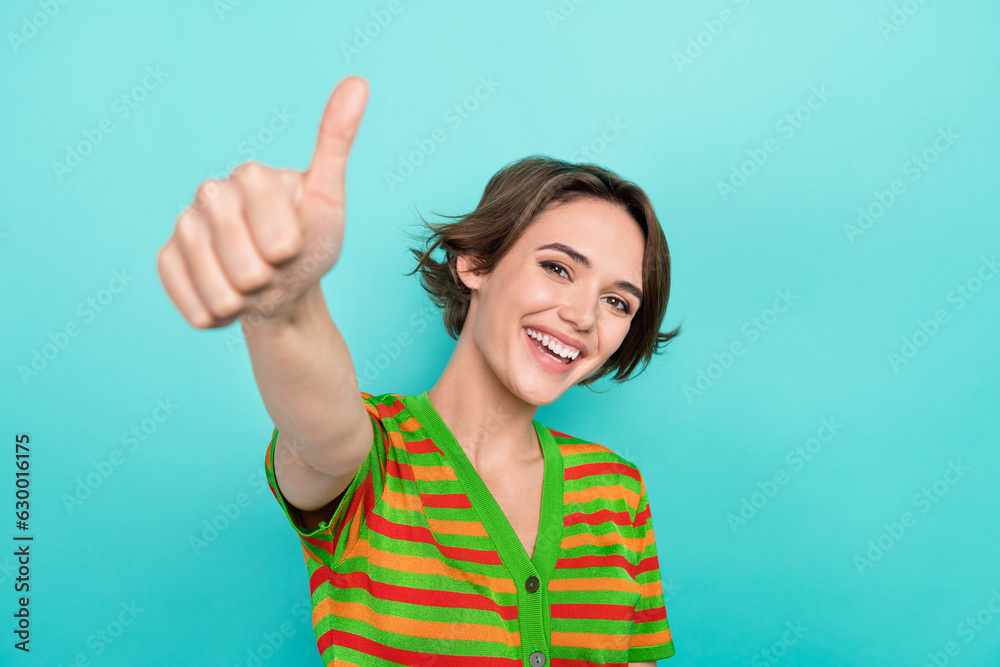 Photo of lovely cheerful girl beaming smile hand finger demonstrate thumb up isolated on teal color background Photo of lovely cheerful girl beaming smile hand finger demonstrate thumb up isolated on teal color background