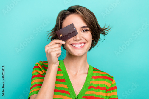 Photo of excited funky woman dressed striped t-shirt holding credit card cover eye isolated turquoise color background