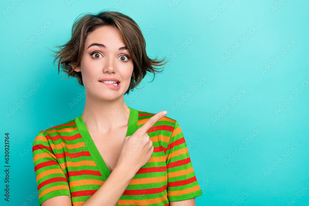 Photo of pretty doubtful lady wear striped cardigan biting lip showing finger empty space isolated teal color background Photo of pretty doubtful lady wear striped cardigan biting lip showing finger empty space isolated teal color background