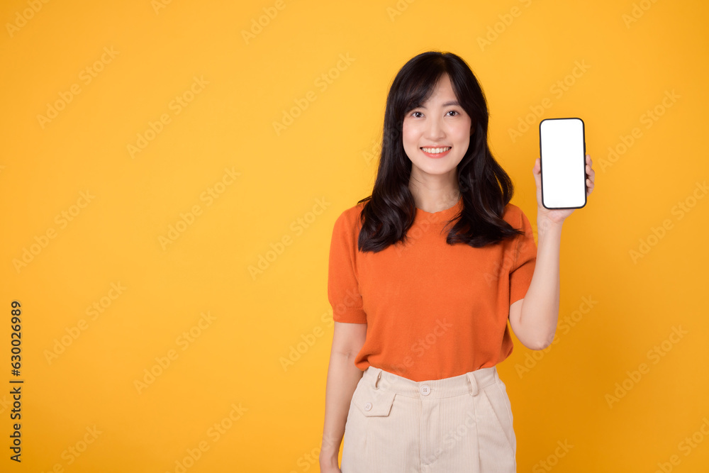 Young asian woman 30s wearing orange shirt showing smartphone blank display screen isolated on yellow background. cheerful happy face female person with new application technology concept. Young asian woman 30s wearing orange shirt showing smartphone blank display screen isolated on yellow background. cheerful happy face female person with new application technology concept.