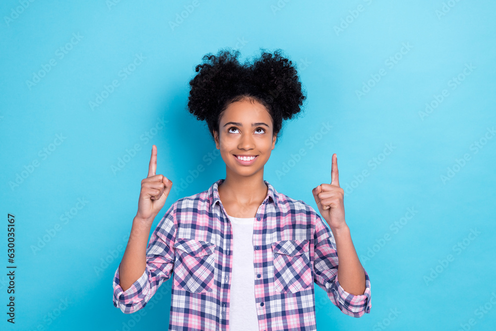 Photo of optimistic nice girl with buns hairstyle wear plaid shirt look directing at sale empty space isolated on blue color background
