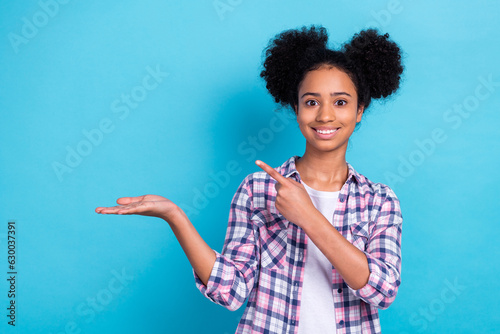 Photo of cute shiny girl dressed plaid shirt holding arm pointing finger holding arm empty space isolated blue color background