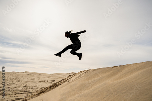 Man jumps dune against the light of the dunes in France © L.Mendizabal
