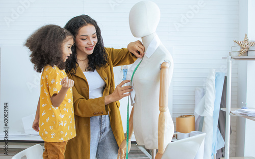 Professional hipster female tailor and daughter measuring mannequin in shop, room, home studio, making, designing fashion dress or clothes. Small Business and Lifestyle Concept.