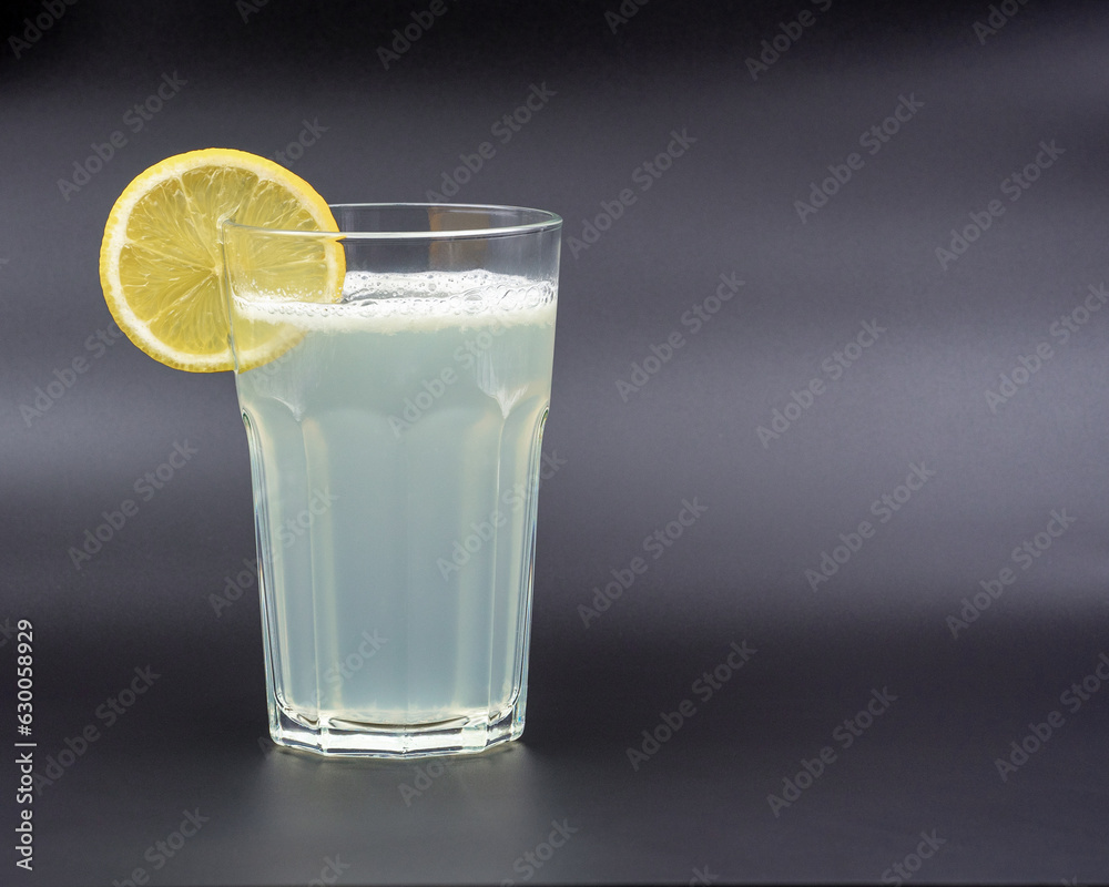 A glass of drink with a slice of lemon on a gray background A glass of drink with a slice of lemon on a gray background