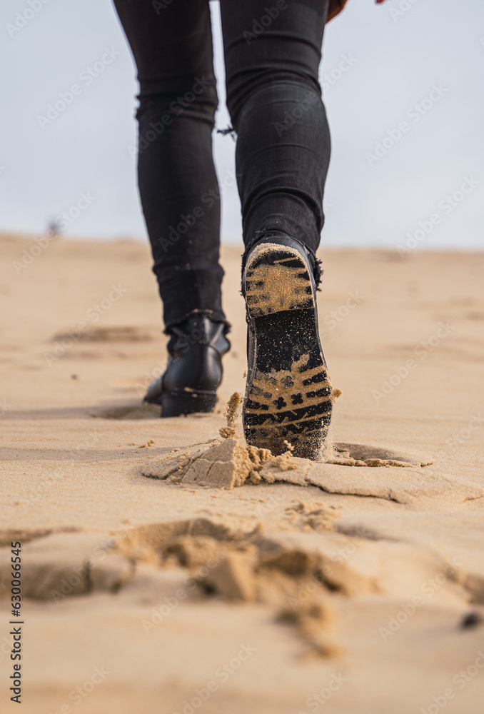 footprints in the sand, in black boots and brown coat, walking in the dunes.