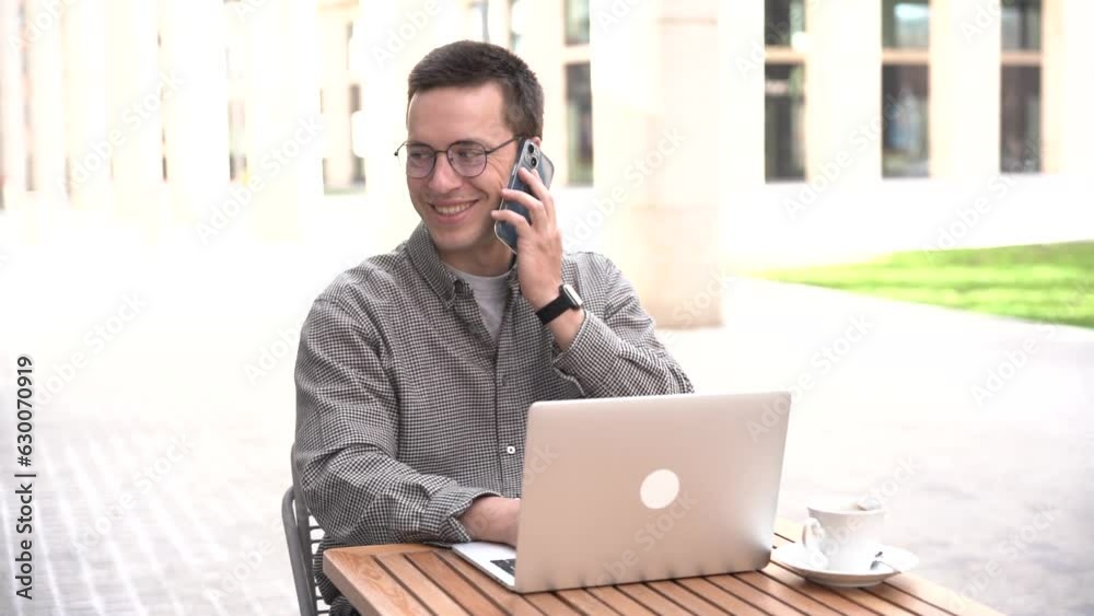 Answers the phone works online remotely sends an email. A happy man is a student. A young male programmer with glasses uses a laptop. Answers the phone works online remotely sends an email. A happy man is a student. A young male programmer with glasses uses a laptop.
