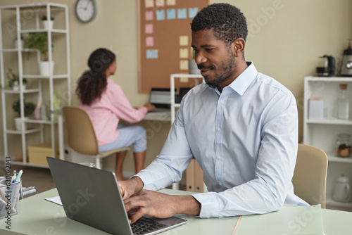 Portrait of adult African American business expert working with laptop at desk in office, copy space