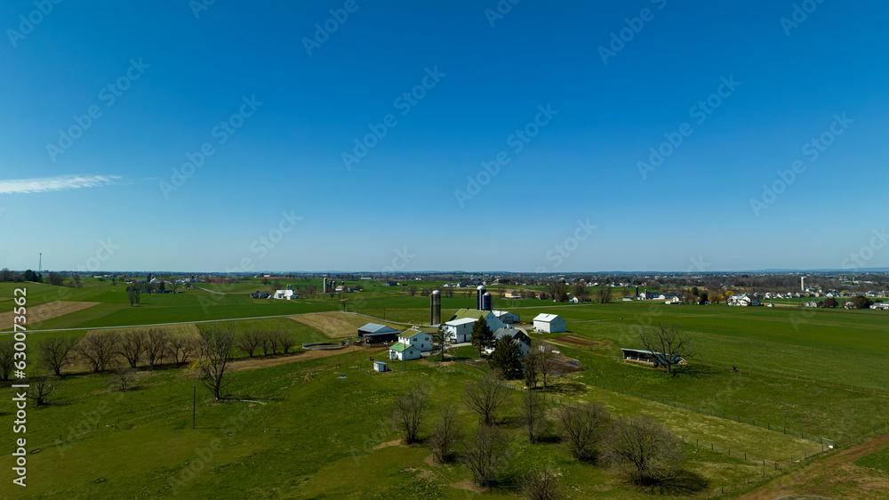 An Aerial View of Countryside, with Farms, Green Crops, Trees, Borders, Barns and Silos. on a Sunny Spring Day