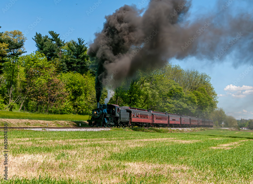 A View of an Antique Restored Steam Passenger Train, Approaching, Blowing Black Smoke, Traveling Thru Rural Countryside on a Sunny Day A View of an Antique Restored Steam Passenger Train, Approaching, Blowing Black Smoke, Traveling Thru Rural Countryside on a Sunny Day