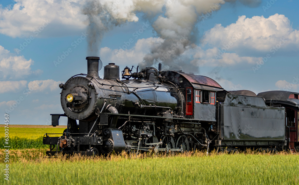 A View of an Antique Steam Passenger Train Approaching, Traveling Thru Rural Countryside, Blowing Smoke, on a Sunny Spring Day
