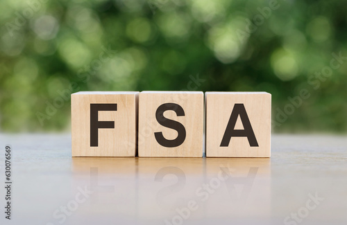 Letters of the alphabet of FSA on wooden cubes, green background. FSA - short for Flexible Spending Account photo