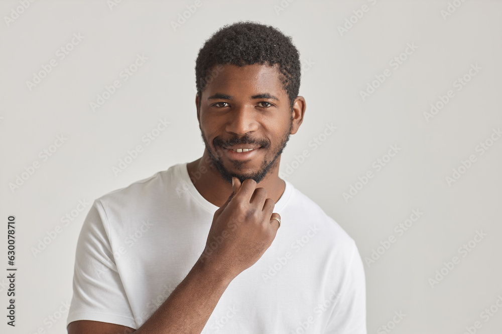 Minimal portrait of confident black man smiling at camera against white background and stroking beard Minimal portrait of confident black man smiling at camera against white background and stroking beard