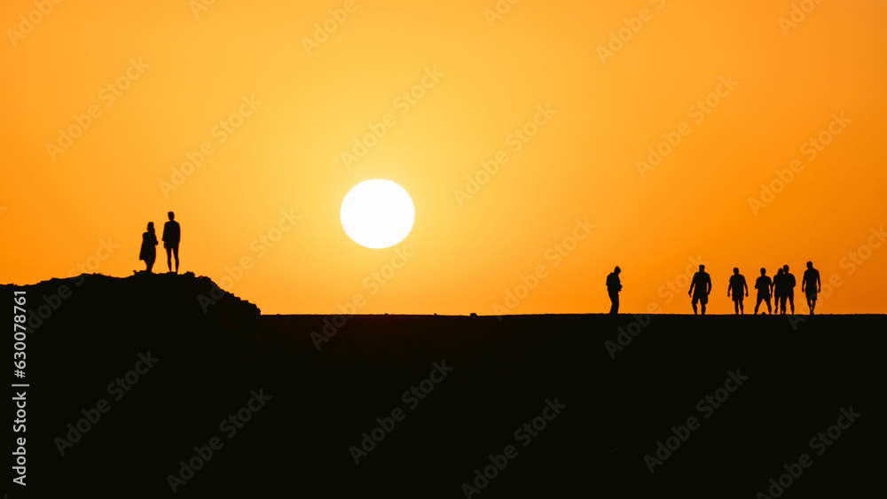 People silhouttes in desert watching big sun going down during epic sunset in Egypt. People silhouttes in desert watching big sun going down during epic sunset in Egypt.
