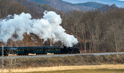 View of a Narrow Gauge Restored Steam Passenger Train Blowing Smoke and Traveling Thru Farmlands on a Winter Day