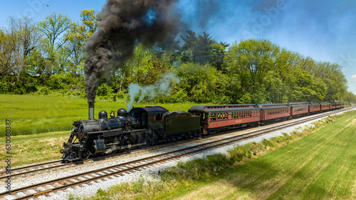 An Aerial View from the Side of An Antique Steam Locomotive and Passenger Coach Stopped and Blowing Smoke and Steam, While Waiting for Passengers to Board on a Sunny Spring Day