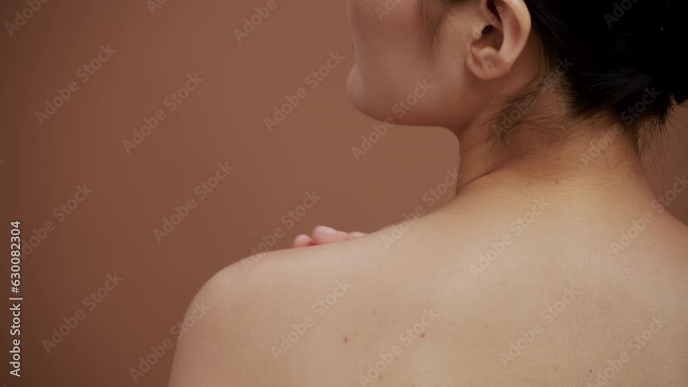 Young woman with clean skin gently touching her own naked shoulder in a back view on a brown background. Concept of skin care for health and beauty Young woman with clean skin gently touching her own naked shoulder in a back view on a brown background. Concept of skin care for health and beauty