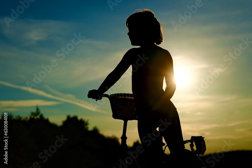 Fototapeta Naklejka Na Ścianę i Meble -  Silhouette of a girl on a bicycle at sunset in a field
