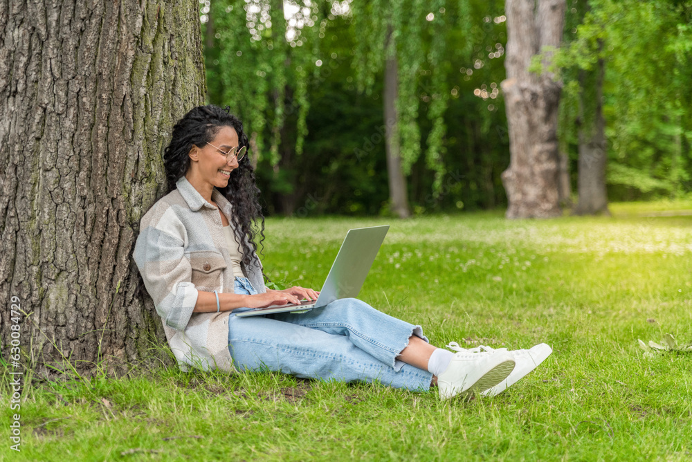 E-learning Concept. Arab Female Student With Laptop Sitting Under Tree In Park, Smiling Young Middle Eastern Woman Study Online On Computer While Relaxing On Green Lawn Outdoors, Copy Space E-learning Concept. Arab Female Student With Laptop Sitting Under Tree In Park, Smiling Young Middle Eastern Woman Study Online On Computer While Relaxing On Green Lawn Outdoors, Copy Space