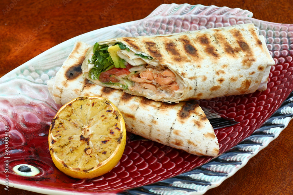 cut grilled salmon fish roll with lemon, garlic sauce, tomato, salad and avocado closeup photo