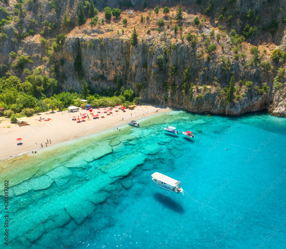 Aerial view of sandy beach, blue sea, yacht and boat, rock, umbrellas at summer sunny day. Butterfly Valley in Oludeniz, Turkey. Top drone view of sea coast, swimming people, clear azure water. Travel