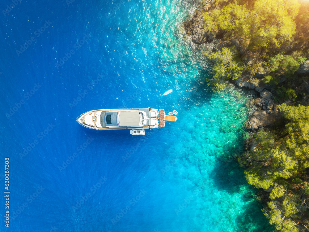 Aerial view of alone beautiful yacht on the sea bay at sunset in summer. Fethiye lagoons, Turkey. Top view of luxury boat, clear blue water, sand, stones and green trees. Tropical landscape. Exotic Aerial view of alone beautiful yacht on the sea bay at sunset in summer. Fethiye lagoons, Turkey. Top view of luxury boat, clear blue water, sand, stones and green trees. Tropical landscape. Exotic