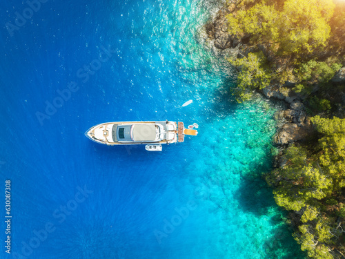 Aerial view of alone beautiful yacht on the sea bay at sunset in summer. Fethiye lagoons, Turkey. Top view of luxury boat, clear blue water, sand, stones and green trees. Tropical landscape. Exotic
