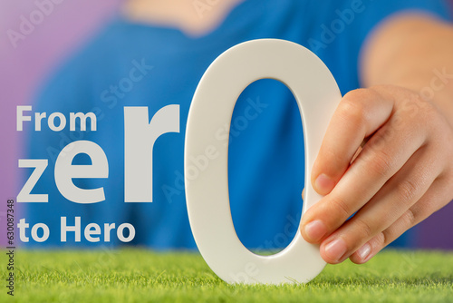 From Zero to Hero. Close-up concept photo of a hand holding a white zero. Motivational text that inspires new achievements and striving for success.