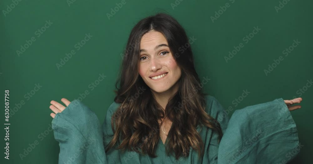 Puzzled confused brunette young woman wearing green dress posing isolated on green color background in studio. Curly hair brunette woman looking camera spreading hands say oops. Puzzled confused brunette young woman wearing green dress posing isolated on green color background in studio. Curly hair brunette woman looking camera spreading hands say oops.
