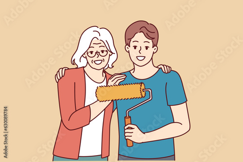 Grandmother hugging grandson doing repairs and using roller to paint walls in apartment and renovate interior. Elderly gray-haired woman near young happy man ready to start repairs in house