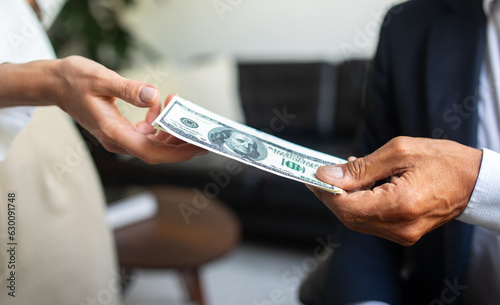 Caucasian old businessman in suit gives money dollars cash to woman hand in office interior, close up