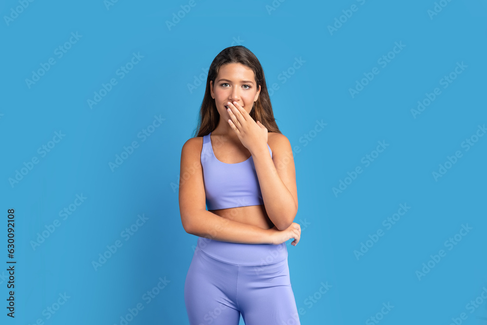 Glad shocked slim young caucasian lady in sportswear covers open mouth with hand after workout Glad shocked slim young caucasian lady in sportswear covers open mouth with hand after workout