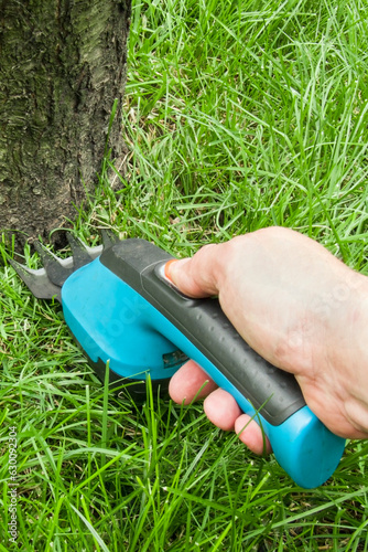 Foto cordless lawn clippers, against the background of a mowed lawn, turquoise color,