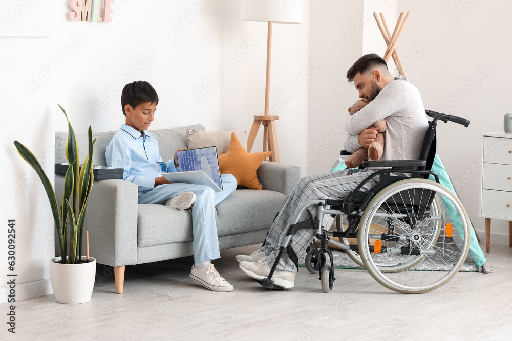 Little boy and his father in wheelchair with toy at home Little boy and his father in wheelchair with toy at home