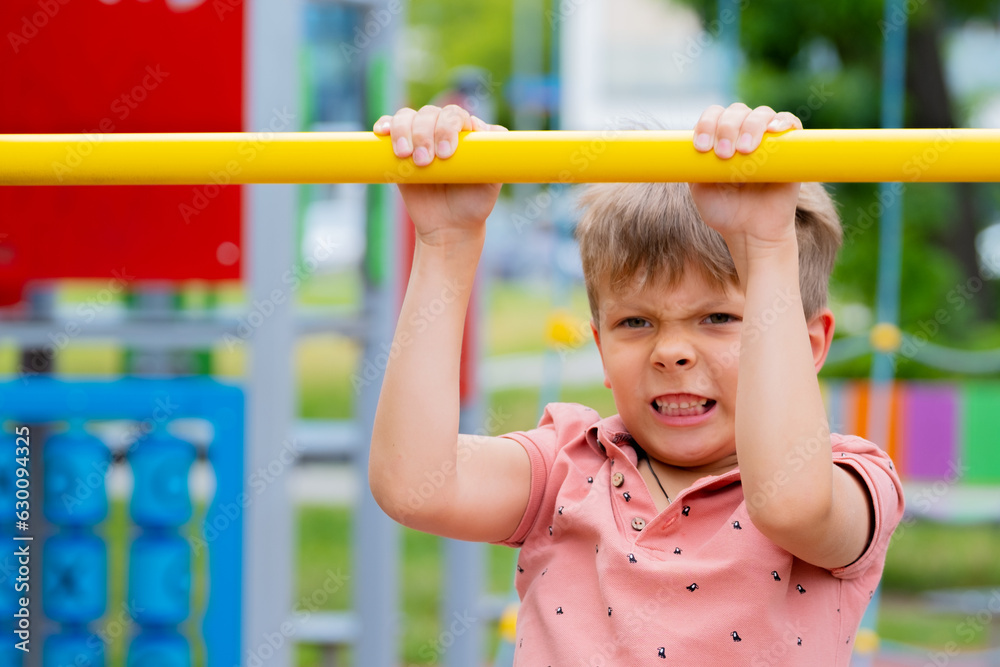 Boy playing sports on street sports ground. Boy pulling himself up on horizontal bar.. Boy playing sports on street sports ground. Boy pulling himself up on horizontal bar..