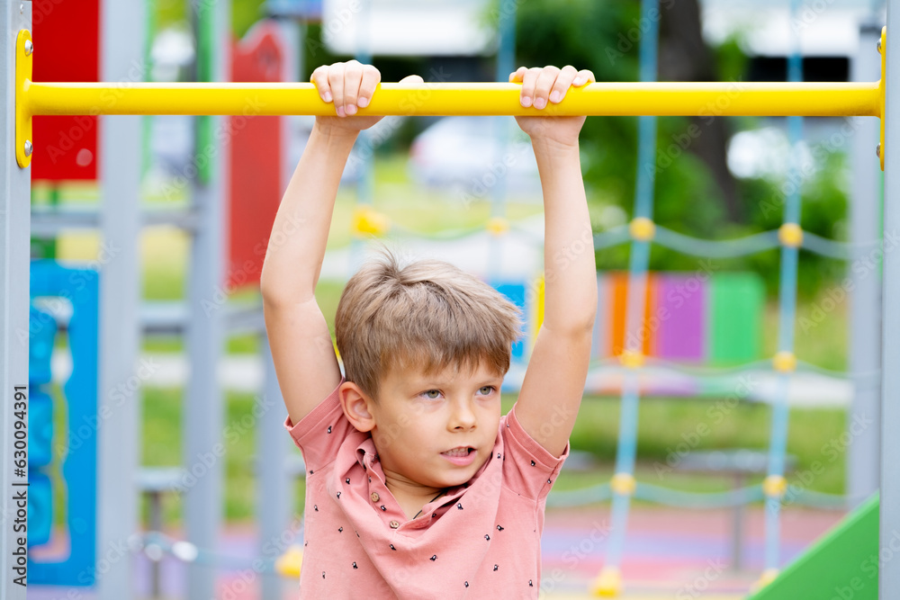 Boy playing sports on street sports ground. Boy pulling himself up on horizontal bar.. Boy playing sports on street sports ground. Boy pulling himself up on horizontal bar..