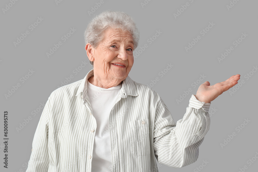 Senior woman showing something on grey background Senior woman showing something on grey background