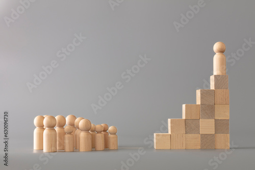 Leader figure standing out from crowd on wooden cubes, other figures in front on floor. Leadership and team. Boss and subordinates. Individual and superiority concept on grey background.