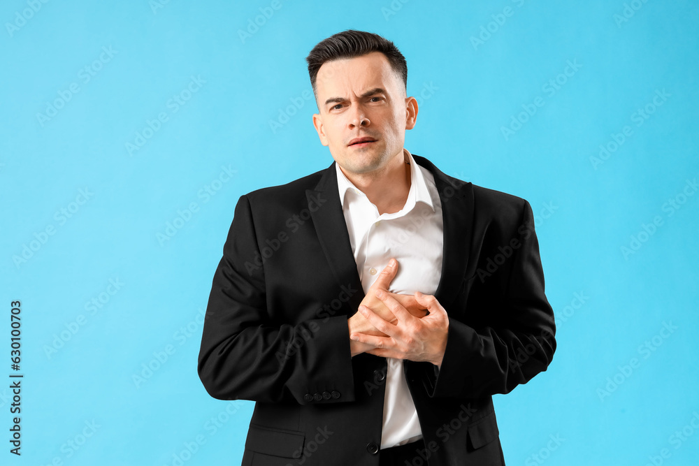 Young businessman having heart attack on blue background Young businessman having heart attack on blue background
