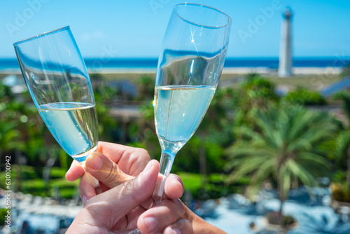 Fotografía Concepto de amor y celebración con copas,  brindis de una pareja en playa o islas en verano bajo el sol con faro a lo lejos