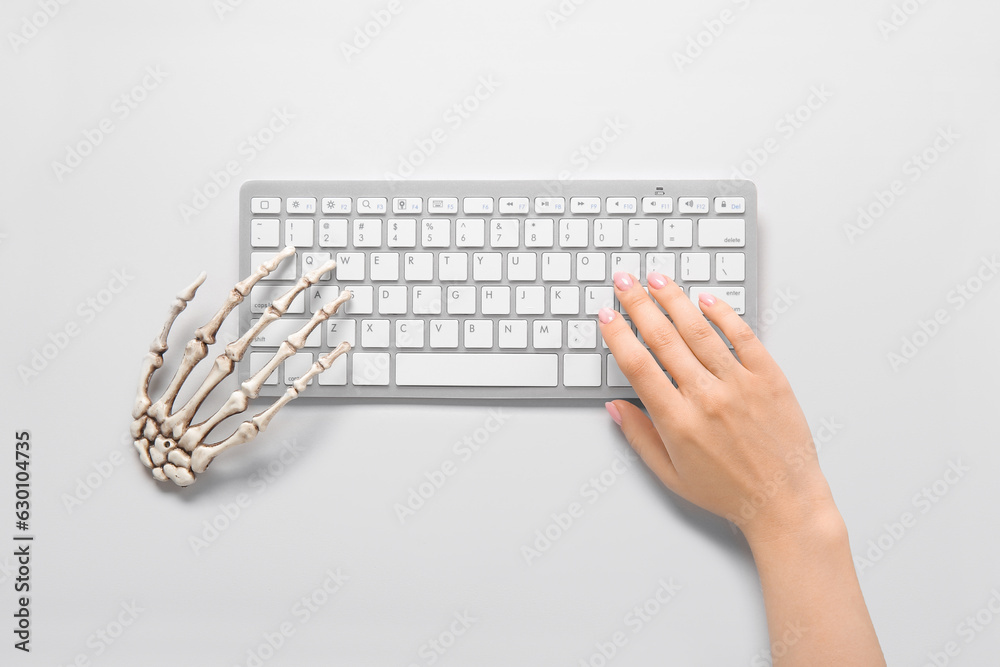 Female and skeleton hands with modern computer keyboard on white background. Halloween celebration