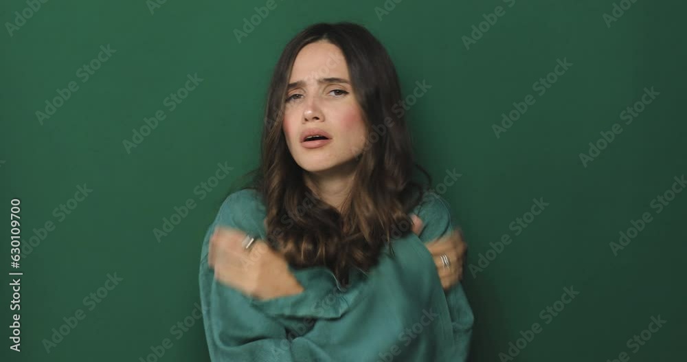 Young woman freezes in dress warms up by hugging herself, seasonal changes low temperature heating problem, looks at camera, chills feeling of coldness concept, isolated on green background. Young woman freezes in dress warms up by hugging herself, seasonal changes low temperature heating problem, looks at camera, chills feeling of coldness concept, isolated on green background.