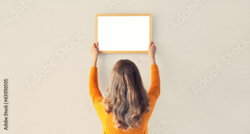 Photos Young woman decorating interior, hanging blank a photo frame mockup on white wal