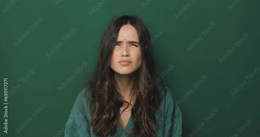 Brunette curly woman squinting trying to see or read text, running eyes standing isolated on green background. Problem with vision. 