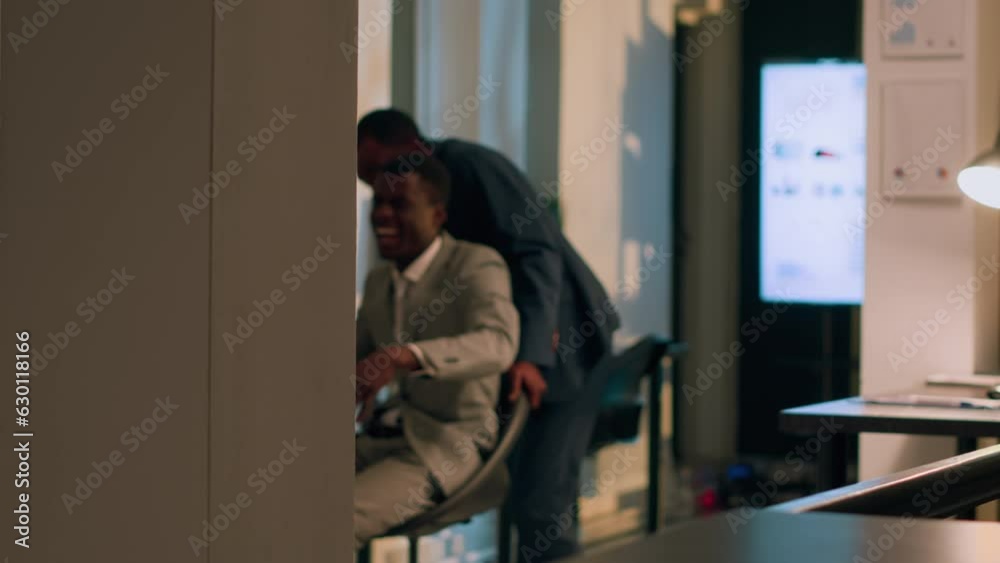 African american employee sliding with chair in office hallway, pretending to be a plane, making coworker laugh. Businessmen entertaining eachother, playing during nightshift African american employee sliding with chair in office hallway, pretending to be a plane, making coworker laugh. Businessmen entertaining eachother, playing during nightshift