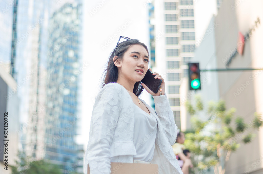 A modern female entrepreneur coordinating with her supplier via the phone while walking though a busy intersection at the city business district.