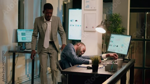 Drowsy accountant sleeping in office, being woken up by colleague shocking him. Worker scaring unsuspecting tired coworker, shaking him up in his desk chair during nightshift
