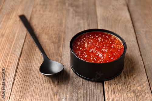 Red salmon caviar in a black tin can and a black spoon on wooden background.