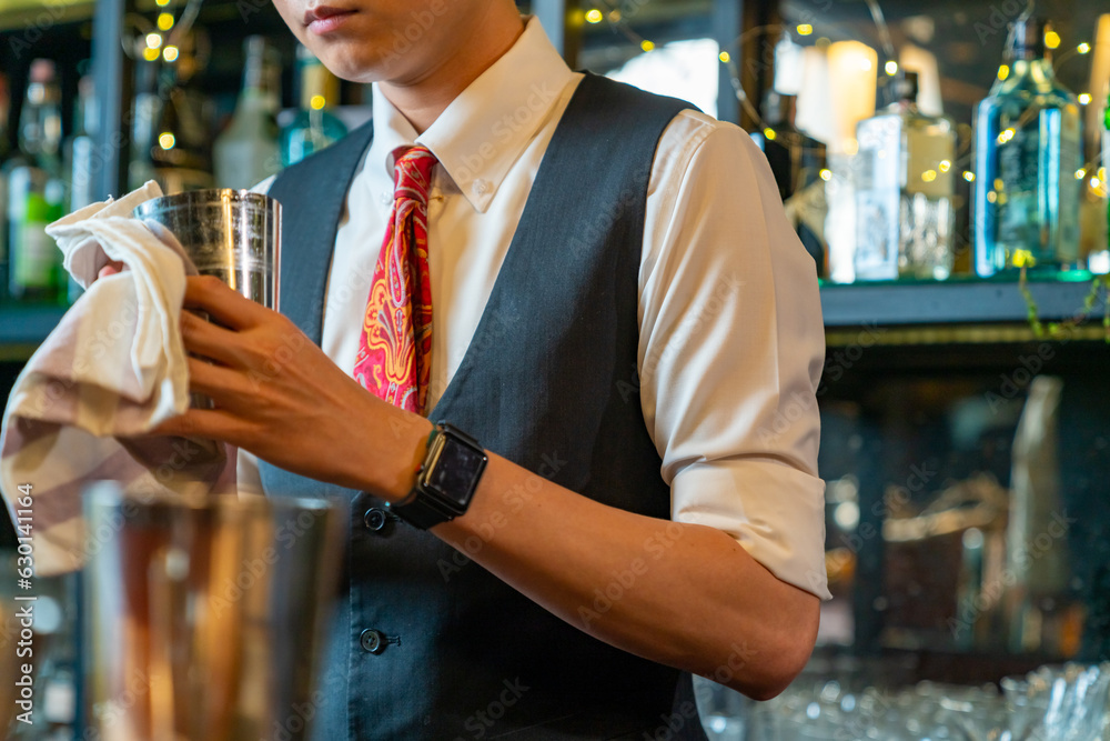 Professional Asian man bartender preparing and serving cocktail drink to customer on bar counter at nightclub. Barman making mixed alcoholic drink for celebrating holiday party at restaurant bar.